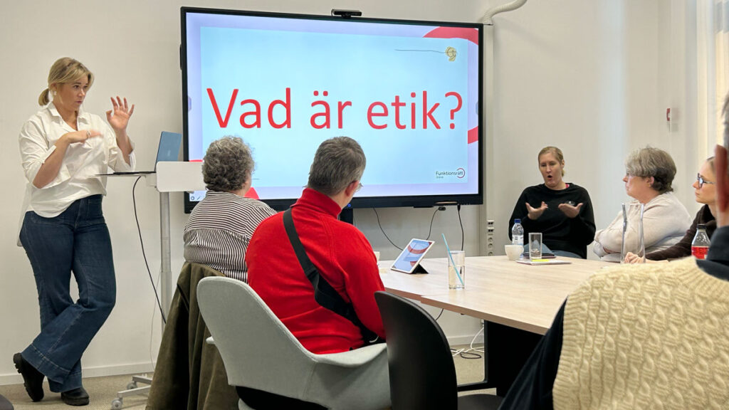 En grupp diskuterar etik framför stor bildskärm. På skärmen står Vad är etik?