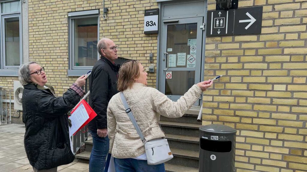 Två kvinnor och en man som pratar och gestikulerar framför en ingång.